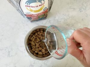 Water being poured into a bowl of Fresh Is Best freeze-dried pork dog food to rehydrate it.